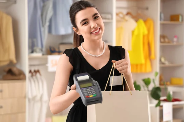 Female sales assistant with payment terminal and shopping bag in boutique