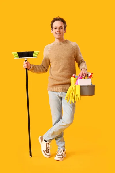 黄色い背景のクリーニング用品のブロムとバケツを持つ若い男 — ストック写真