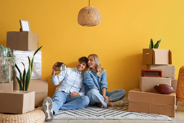 Happy young couple with house model sitting in room on moving day