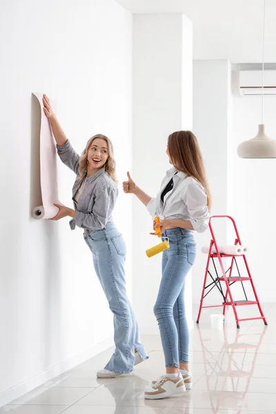 Young women gluing wallpaper at home
