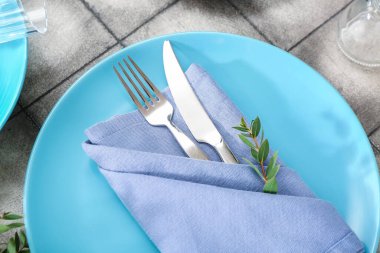 Katlanmış peçete, çatal bıçak takımı ve gri fayanslı bitki dalı olan tabaklar.