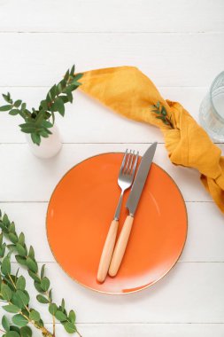 Katlanmış peçete, çatal bıçak takımı ve beyaz ahşap arka planda cam tabaklar.