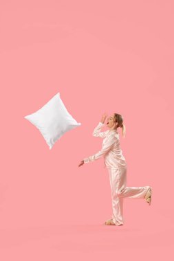 Pembe arka plana yastık atan pijamalı genç bir kadın.