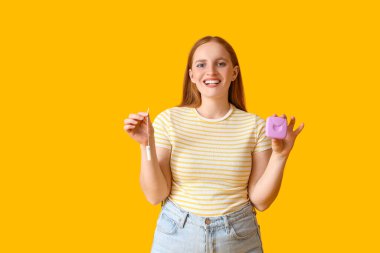 Sarı arka planda tamponu ve kutusu olan genç bir kadın.