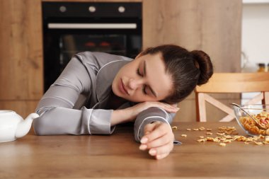 Genç bir kadın mutfakta kahvaltıda uyuyor.