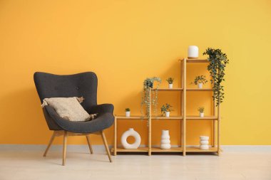 Yastıklı koyu gri koltuk, raf ünitesi ve turuncu duvarın yanındaki ev bitkileri.
