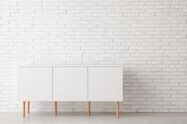 Odanın hafif tuğlalı duvarının yanındaki beyaz çekmeceler.