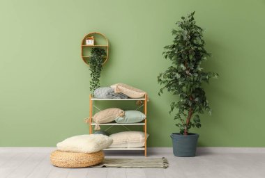 Yastıklı, battaniyeli, çiçekli ve yeşil duvarlı şık ahşap raf ünitesi.