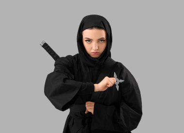 Gri arkaplanda shuriken olan kadın ninja.