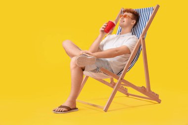 Elinde soda olan genç adam sarı arka planda iskemlede dinleniyor.