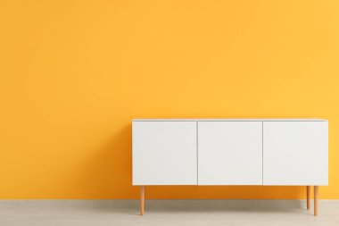 Turuncu duvarın yanındaki beyaz çekmeceler şık.