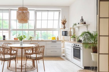 Beyaz tezgahlı, yemek masalı ve büyük pencereli aydınlık mutfağın içi.