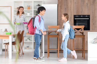 Anne mutfakta küçük çocuklarına beslenme çantası veriyor.