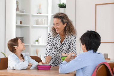 Anne mutfakta küçük çocuklarına beslenme çantası veriyor.