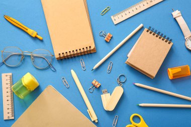 Farklı okul kırtasiyesi, mavi arka planda not defterleri ve gözlükler
