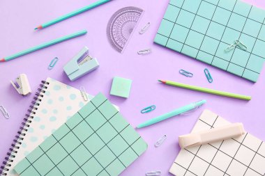 Farklı okul kırtasiyesi ve mor arkaplan üzerine not defterleri