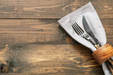 Kahverengi ahşap arka planda peçeteli modern gümüş çatal bıçak.