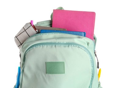 Beyaz arka planda not defterleri ve kurşun kalemlerle dolu yeşil okul çantası.