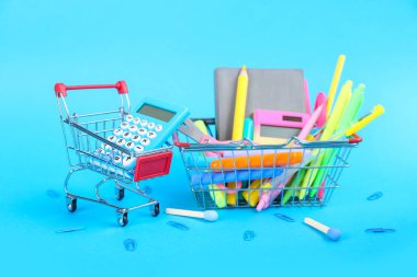 Alışveriş arabası ve sepet mavi arka planda farklı kırtasiye malzemesi.