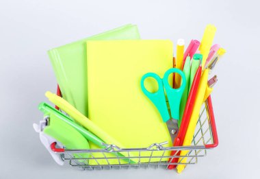 Beyaz arka planda farklı kırtasiye malzemesi olan alışveriş sepeti