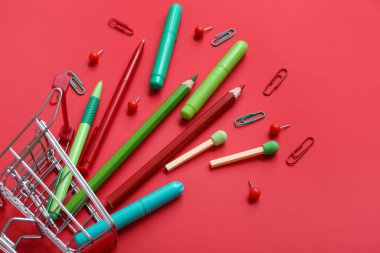 Kırmızı arka planda farklı kırtasiye malzemesi olan alışveriş arabası.