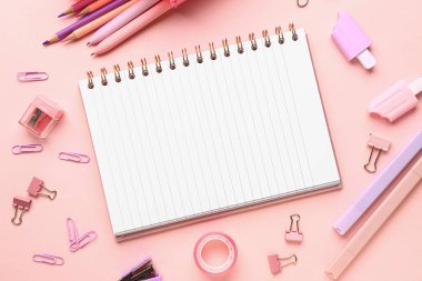Pembe arka planda farklı kırtasiye malzemesi içeren defter.