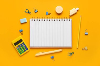 Turuncu arka planda farklı kırtasiye malzemesi içeren defter