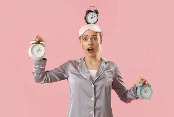 Young woman in pajamas with alarm clocks on pink background