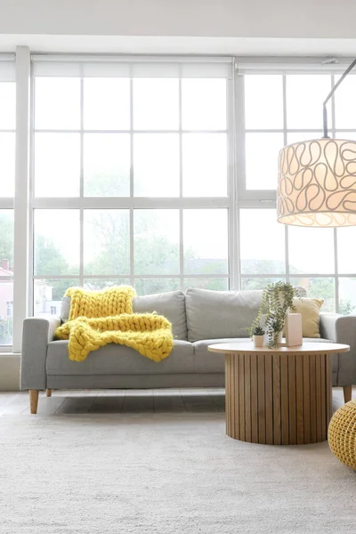 Işıl ışıl oturma odasının içinde rahat gri kanepe, sehpa ve büyük pencerenin yanında parlayan lamba.