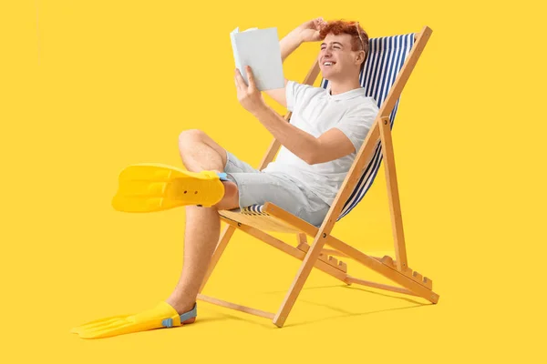 黄色の背景にデッキチェアで本を読んでいる若い男 — ストック写真