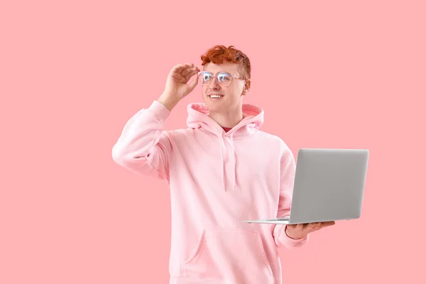 ピンクの背景にラップトップを持つ若い赤毛の男 — ストック写真