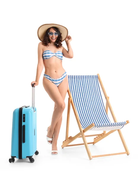 Young woman with suitcase and deck chair on white background
