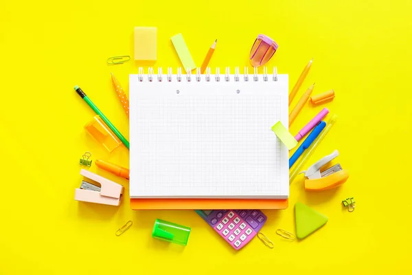 黄色の背景に白いノートと学校の文房具が付いている構成 — ストック写真