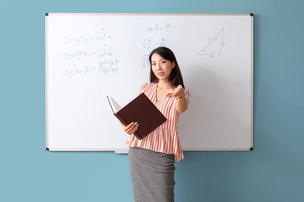 教室のフリップボード近くの本を持つアジアの数学の教師 — ストック写真