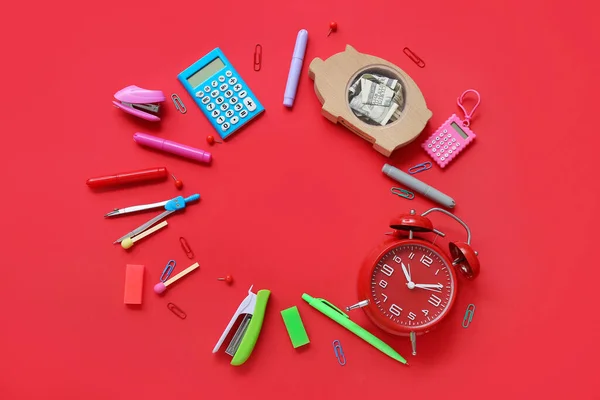 Alarm clock, wooden piggy bank with money and different stationery on red background