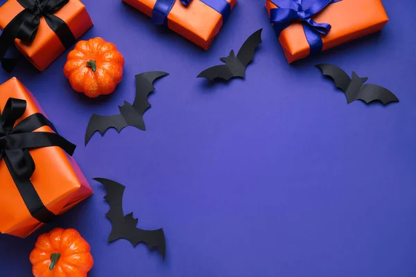 Composition with gift boxes, pumpkins and paper bats for Halloween on blue background