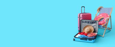 Güverte sandalyesi, bavullar ve açık mavi arka planda plaj aksesuarları.