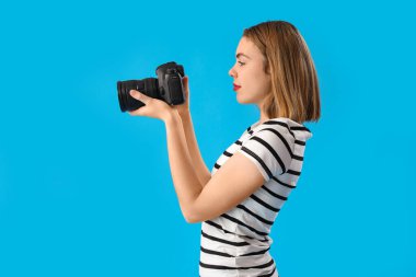 Mavi arka planda profesyonel kamerası olan kadın fotoğrafçı.