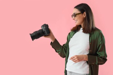 Pembe arka planda profesyonel kamerası olan kadın fotoğrafçı.