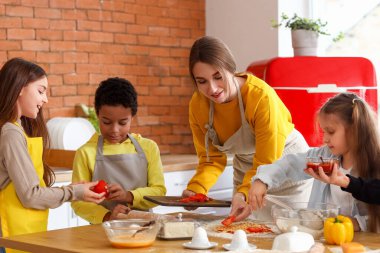 Mutfakta aşçılık kursu sırasında pizza hazırlayan bir grup küçük çocukla birlikte kadın şef.