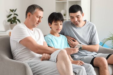 Babası ve dedesiyle mutlu küçük çocuk evde cep telefonu kullanıyor.