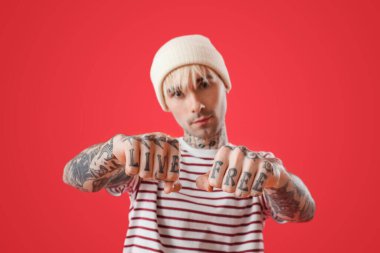 Dövmeli genç adam kırmızı arka planda yumruklarını gösteriyor, yakın plan.