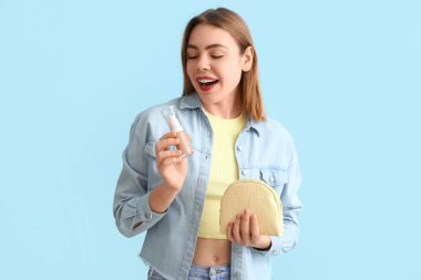 Makyaj temeli ve mavi arka planda makyaj çantası olan genç bir kadın.