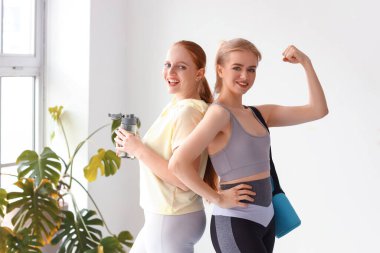Spor salonunda bir şişe su ve yoga minderiyle genç kadınların portresi.