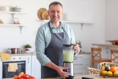 Olgun adam mutfakta blender ile smoothie yapıyor.