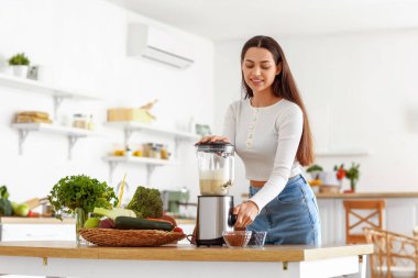 Genç bir kadın mutfakta blender ile sağlıklı smoothie yapıyor.
