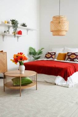 Ahşap masadaki vazoda lale çiçekleri olan şık bir yatak odası.