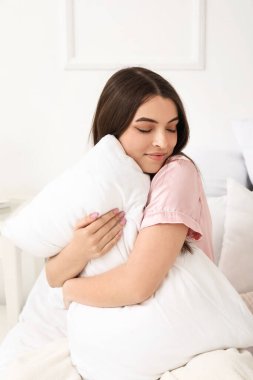 Yumuşak yastıklı güzel bir kadın yatakta oturuyor.