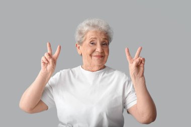 Yaşlı kadın gri arka planda zafer jesti gösteriyor.