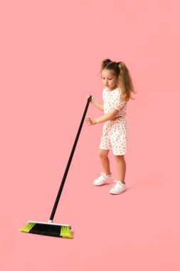 Pembe arka planda süpürgeyle süpürülen tatlı küçük kız.